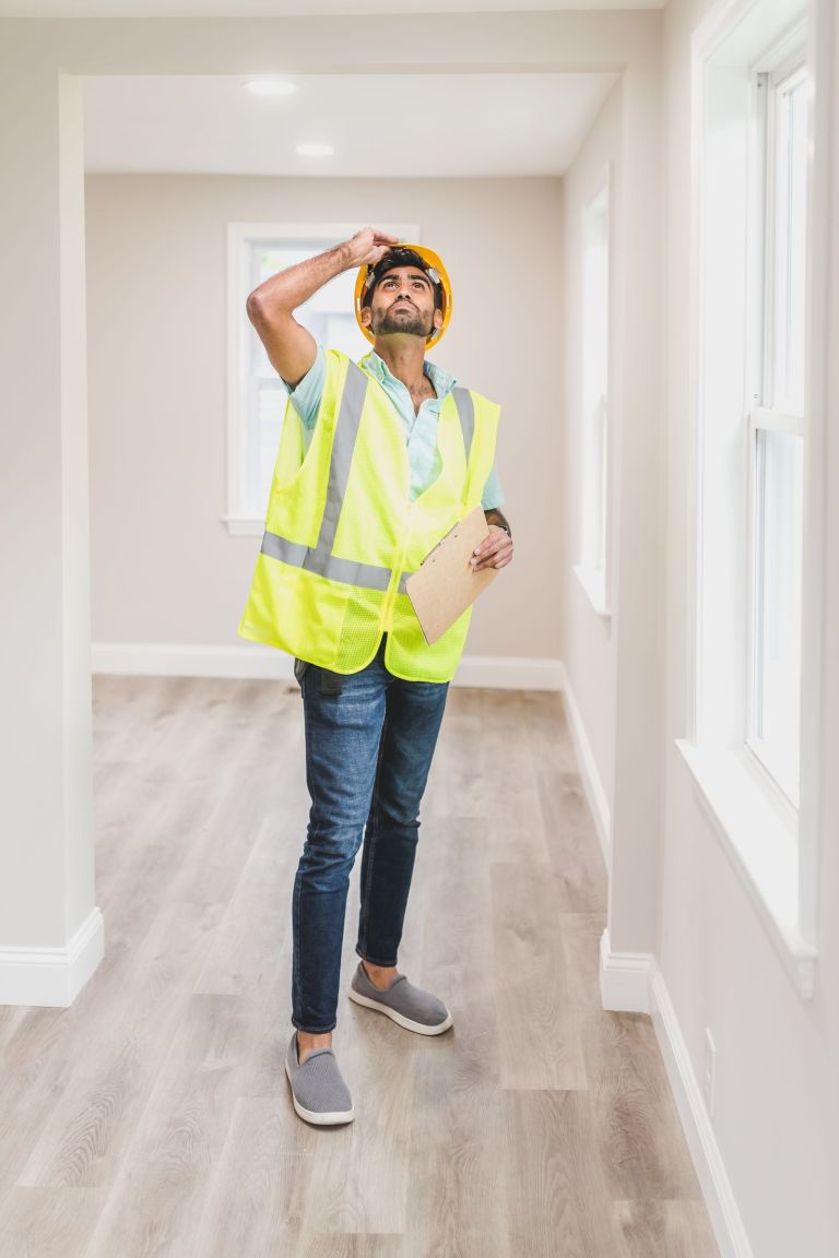 Ein Bauhandwerker mit Helm und Klemmbrett prüft die Decke in einem leeren Haus