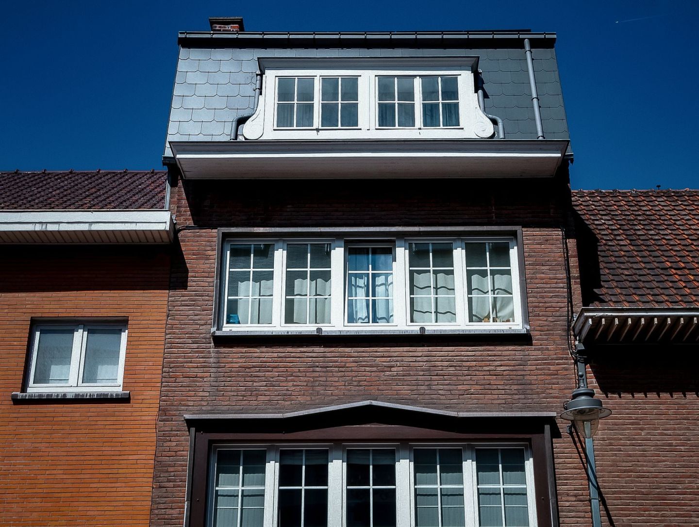Ziegeldach eines Wohnhauses mit verschieferter Gaube vor tiefblauem Himmel