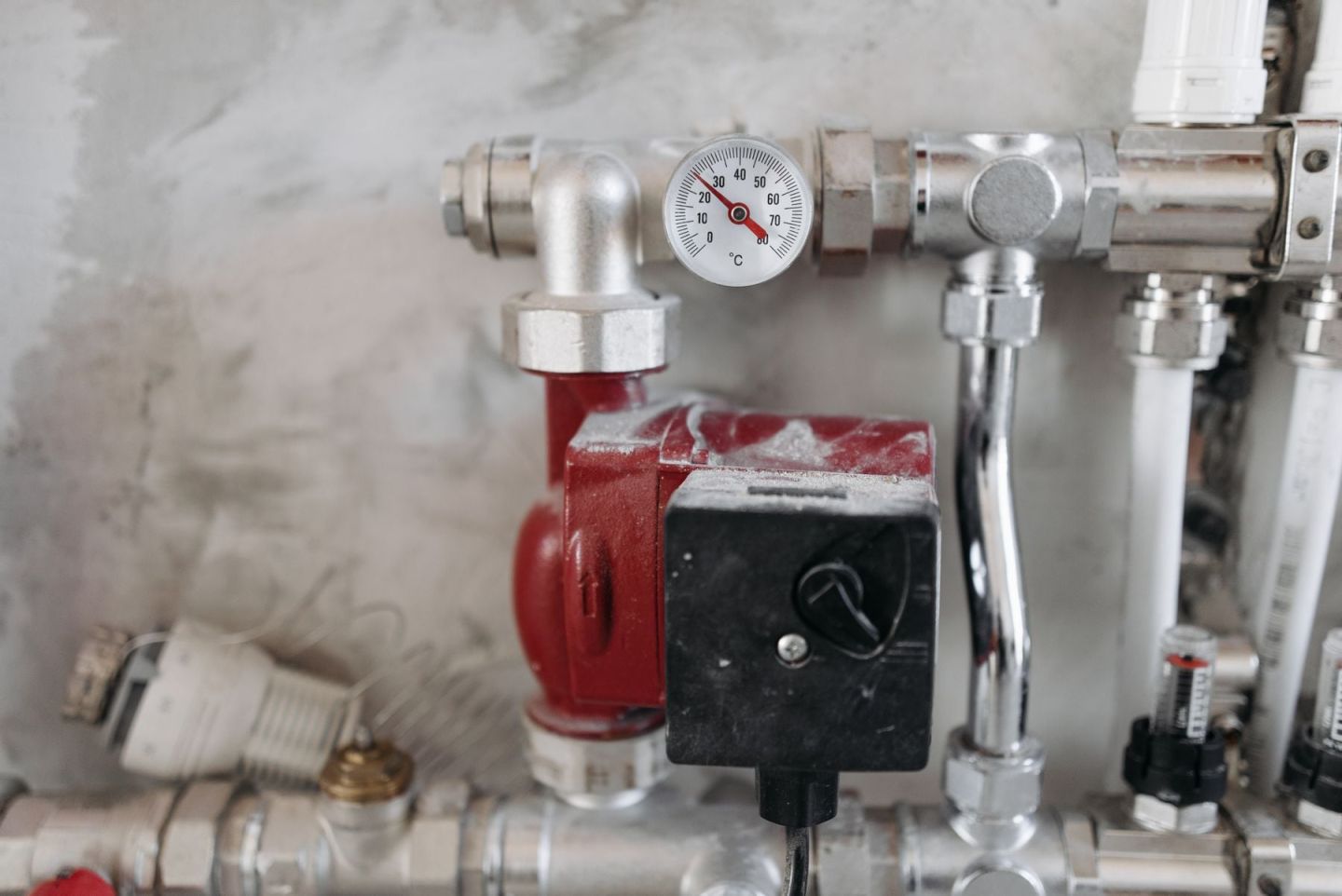 Heizungsverteiler mit Thermometer, Pumpe und Absperrventilen an einer Kellerwand