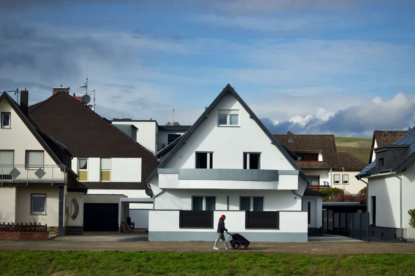 Wohnstraße mit einem hell verputzten Einfamilienhaus und älterer Nachbarbebauung